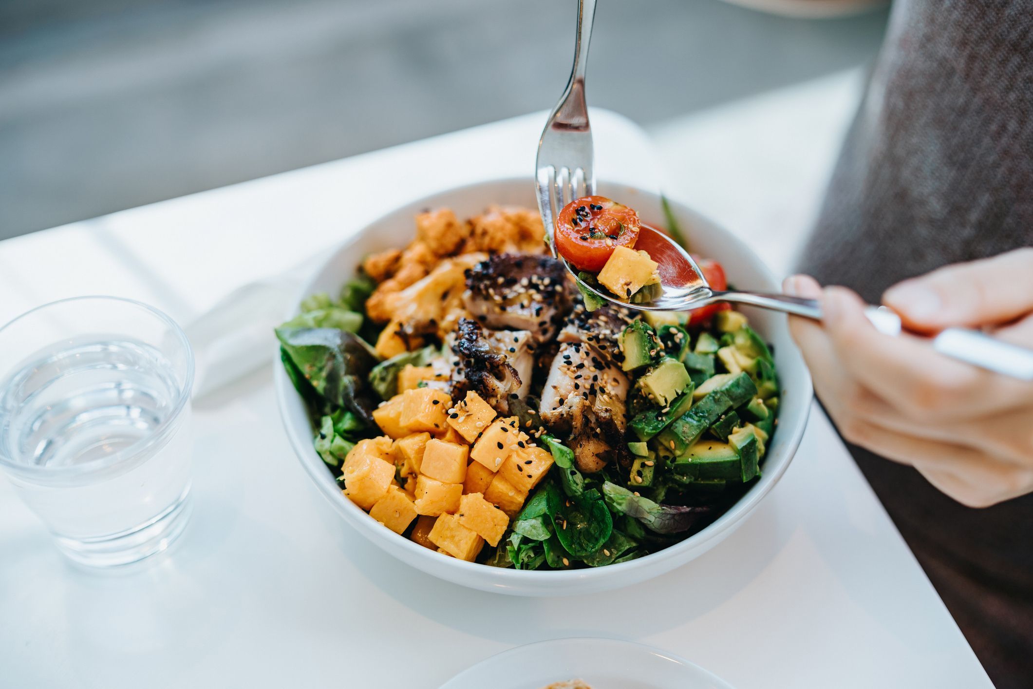 Tigela com salada, legumes, frango, frutas e um copo d'água ao lado