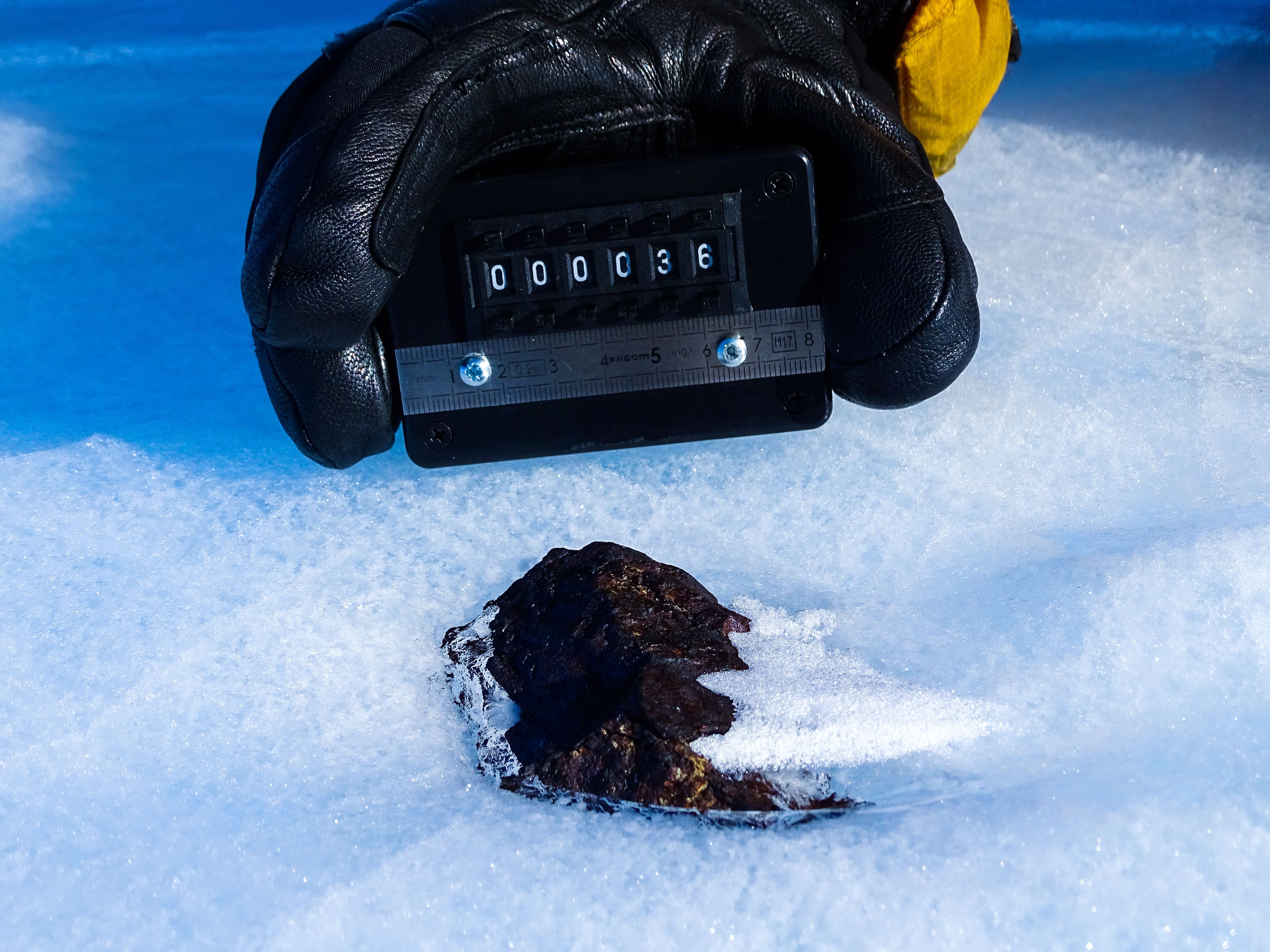 Meteorito antártico (HUT 18036) parcialmente no gelo, em contraste com a maioria das amostras que são coletadas enquanto estão na superfície; meteorito coletado pelo projeto Lost Meteorites of Antarctica (crédito: Katherine Joy, The University of Manchester, The Lost Meteorites of Antarctica project)