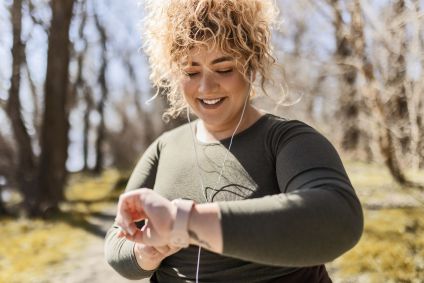 Jovem mulher com excesso de peso com fones de ouvido olhando para o relógio em um parque