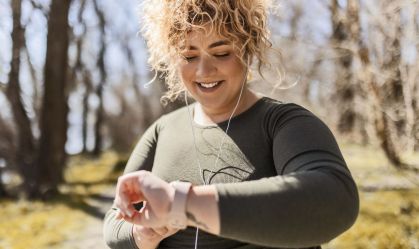 Jovem mulher com excesso de peso com fones de ouvido olhando para o relógio em um parque