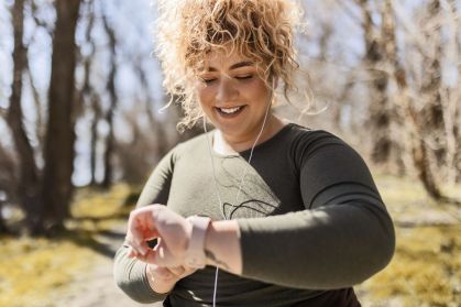 Jovem mulher com excesso de peso com fones de ouvido olhando para o relógio em um parque