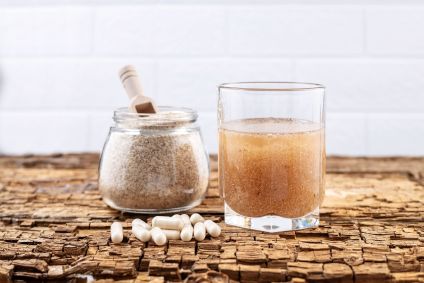 Cápsulas de psyllium e um copo de água e casca de psyllium em uma tábua de madeira velha