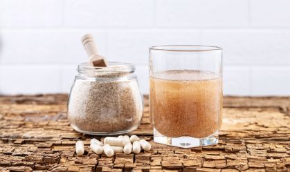 Cápsulas de psyllium e um copo de água e casca de psyllium em uma tábua de madeira velha