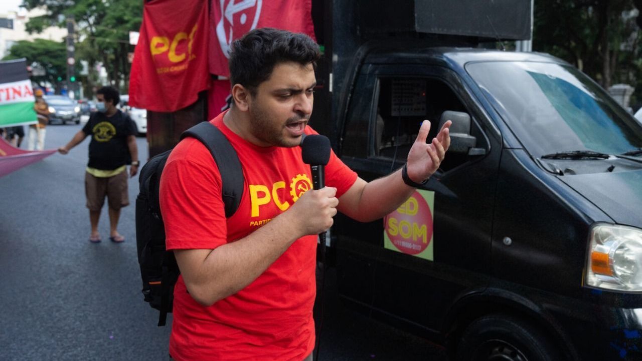 Foto mostra João Pimenta com uma camisa vermelha discursando na rua próximo a um caminhão