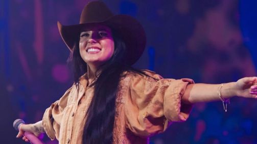 Foto da cantora Ana Castela com os braços abertos enquanto sorri no palco