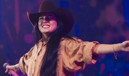 Foto da cantora Ana Castela com os braços abertos enquanto sorri no palco