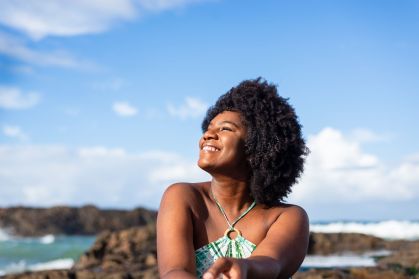 Retrato de mulher de pele negra e cabelos cacheados escuros sorrindo e olhando para o céu