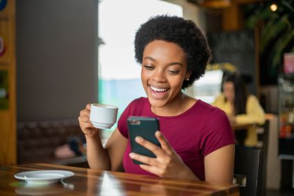 Mulher feliz olhando para seu celular enquanto bebe uma xícara de café em um café