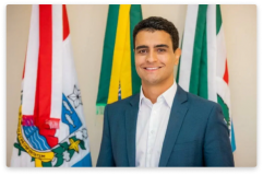 Foto mostra o prefeito João Henrique Caldas. Ele é branco, veste terno azul e camisa branca. Ele sorri.