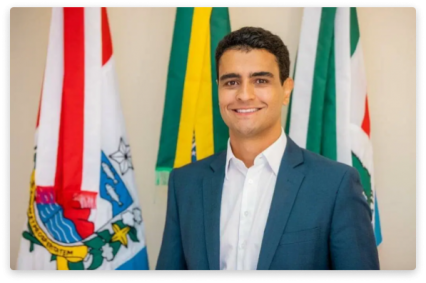 Foto mostra o prefeito João Henrique Caldas. Ele é branco, veste terno azul e camisa branca. Ele sorri.