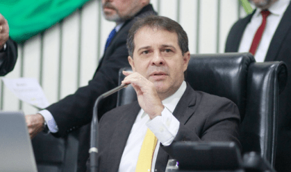 Na foto, Evandro Leitão aparece segurando um microfone. Ele veste um terno preto, gravata amarela e camisa branca.