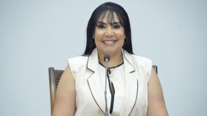 Janad Valcari é branca e tem cabelo preto e liso. Usa roupa branca e sorri.