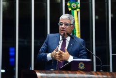Eduardo Girão veste terno azul escuro e gravata roxa. Tem cabelo branco e usa óculos.