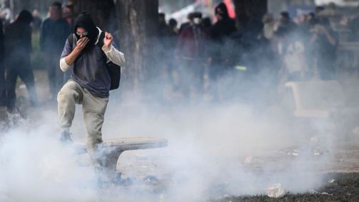 Manifestante tenta escapar do gás lacrimogêneo durante um protesto contra um o megaprojeto de lei do governo do presidente Milei que está sendo debatido no Congresso da Argentina