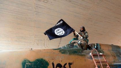 Combatente do Estado Islâmico com uma bandeira enquanto está em um caça do governo capturado em Raqqa, Síria, em 2015