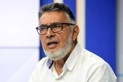 Geraldo Carvalho tem barba branca e cabelo grisalho. Veste camistea branca e usa óculos.