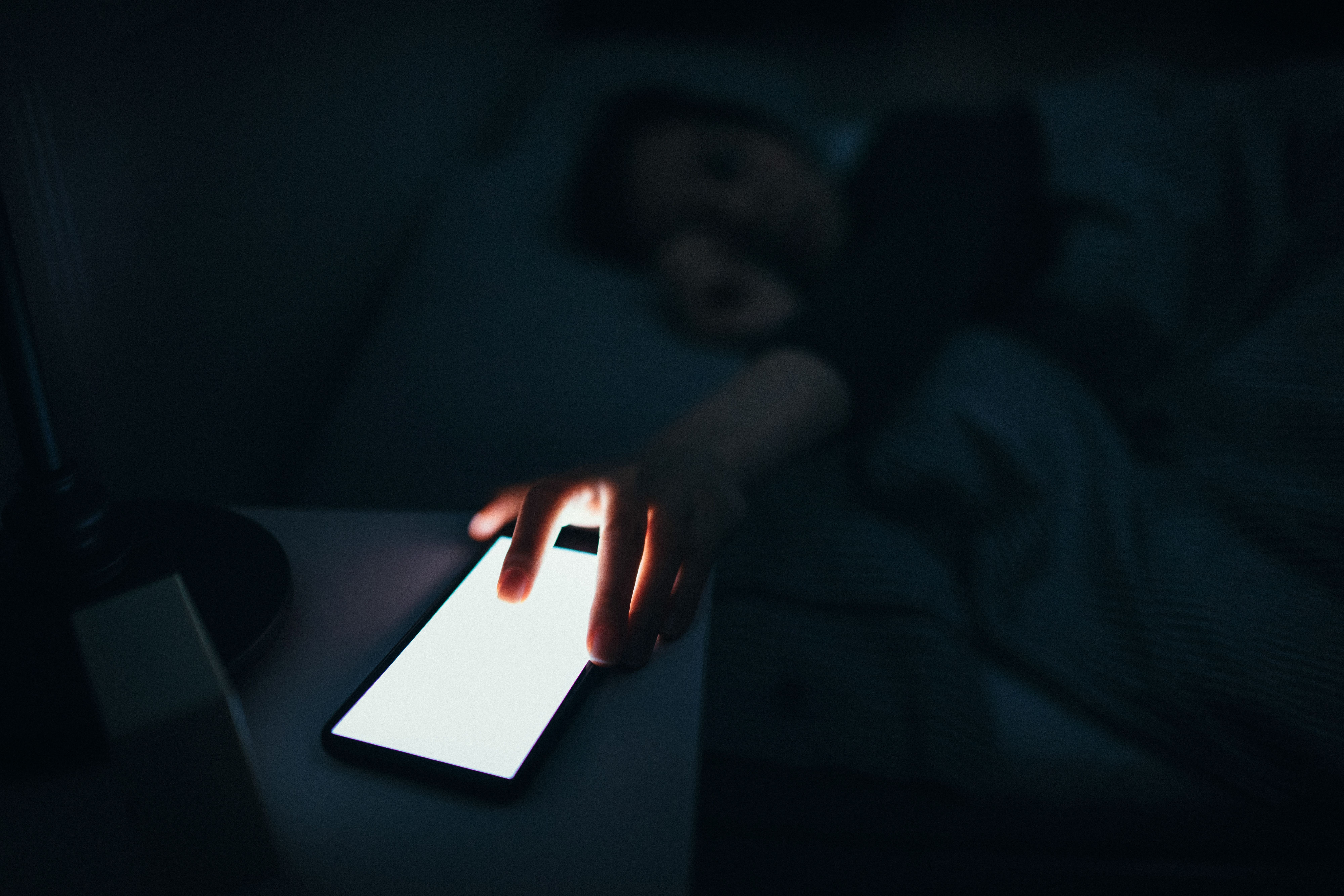 Woman reaching and switching off disturbing calls from work on smartphone while sleeping at midnight