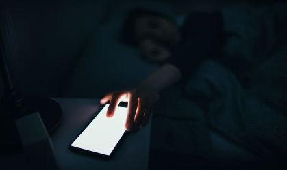 Woman reaching and switching off disturbing calls from work on smartphone while sleeping at midnight