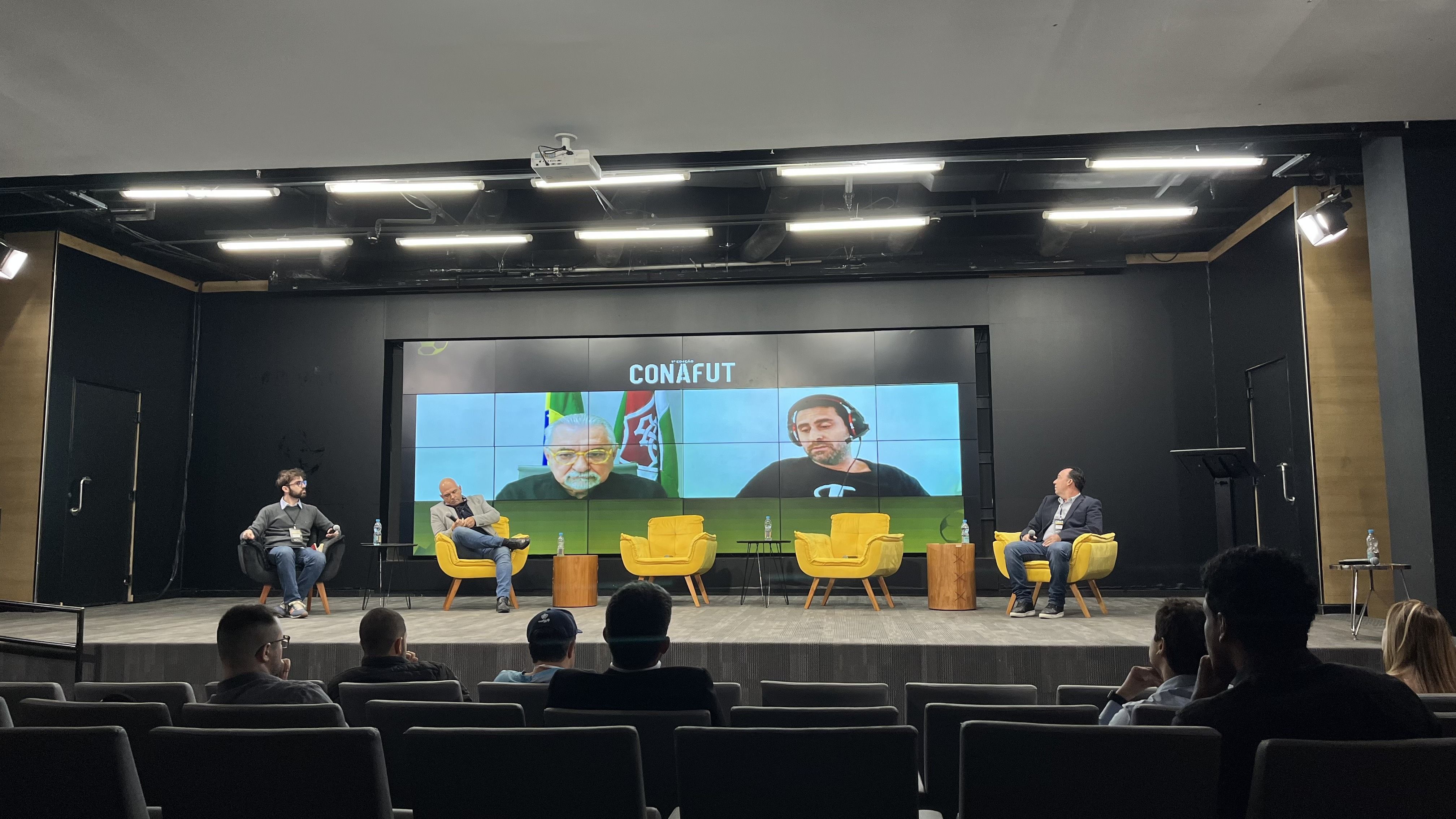 Painel sobre a presença de técnicos estrangeiros no futebol brasileiro. No palco, da esq. para a dir.: Bruno Rodrigues (mediador), Carlos Leiria (Resende-RJ) e Leandro Mehlich (Rio Branco-SP). No telão, Paulo Angioni (Fluminense) e Leonardo Samaja (ATFA)