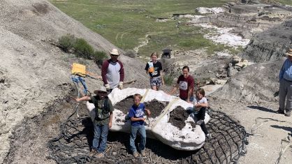 Família que encontrou o fóssil (no sentido horário a partir do canto superior esquerdo: Sam Fisher, Emalynn Fisher, Danielle Fisher, Liam Fisher, Kaiden Madsen e Jessin Fisher) posando com estrutura de gesso após ser colocada em uma rede de helicóptero