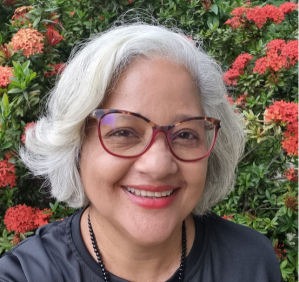Lenilda Luna tem cabelos brancos curtos, usa batom vermelho e óculos e veste uma blusa preta