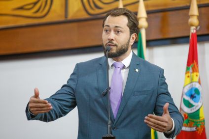 Emerson Jarude é branco e tem cabelo preto. Veste terno azul, camiseta branca e gravata lilás.
