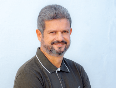 Saulo Arcangeli é branco, tem barba e cabelos grisalhos e sorri.