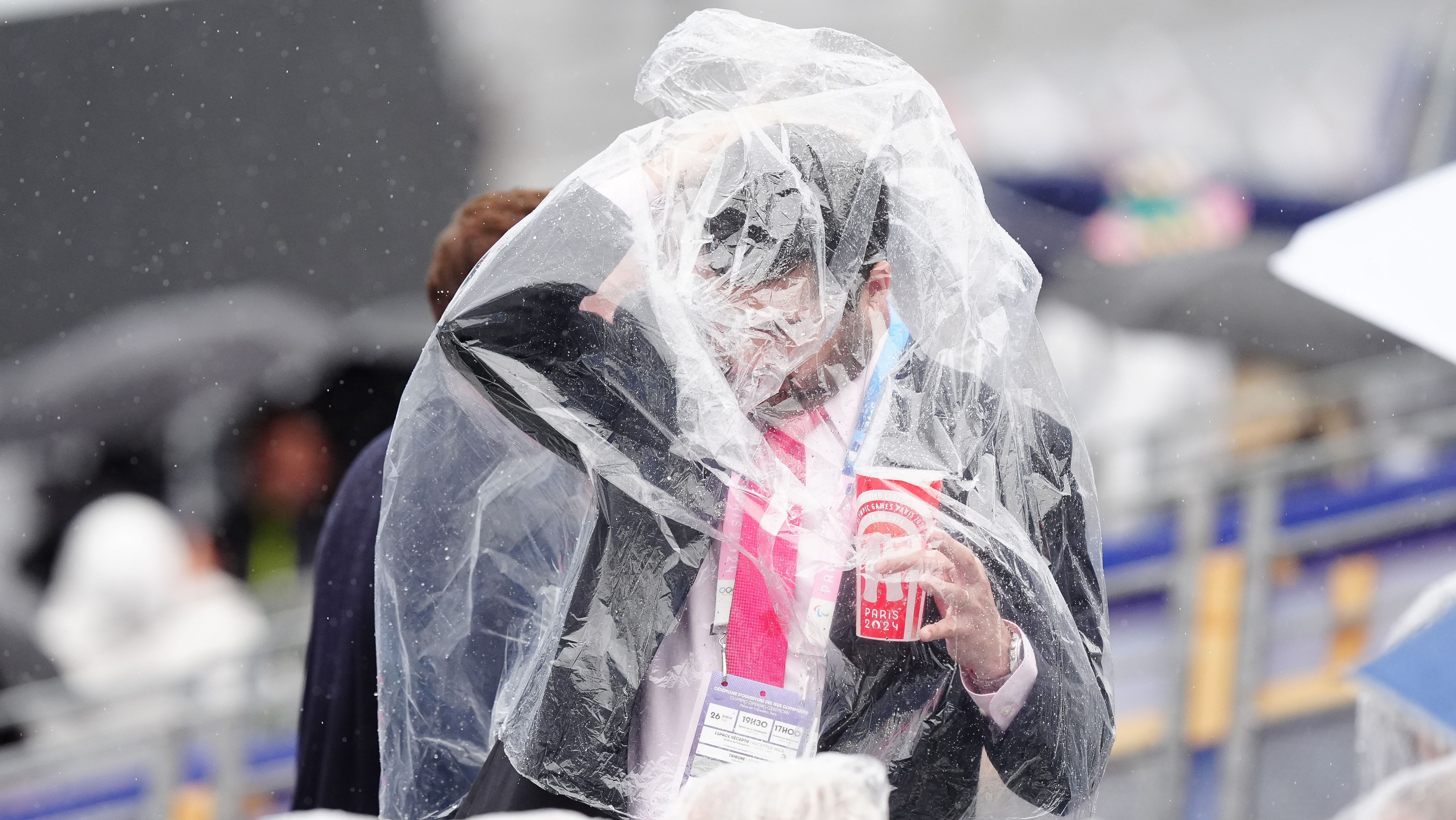Homem se enrola ao tentar vestir uma capa de chuva na cerimônia de abertura da Olimpíada de Paris