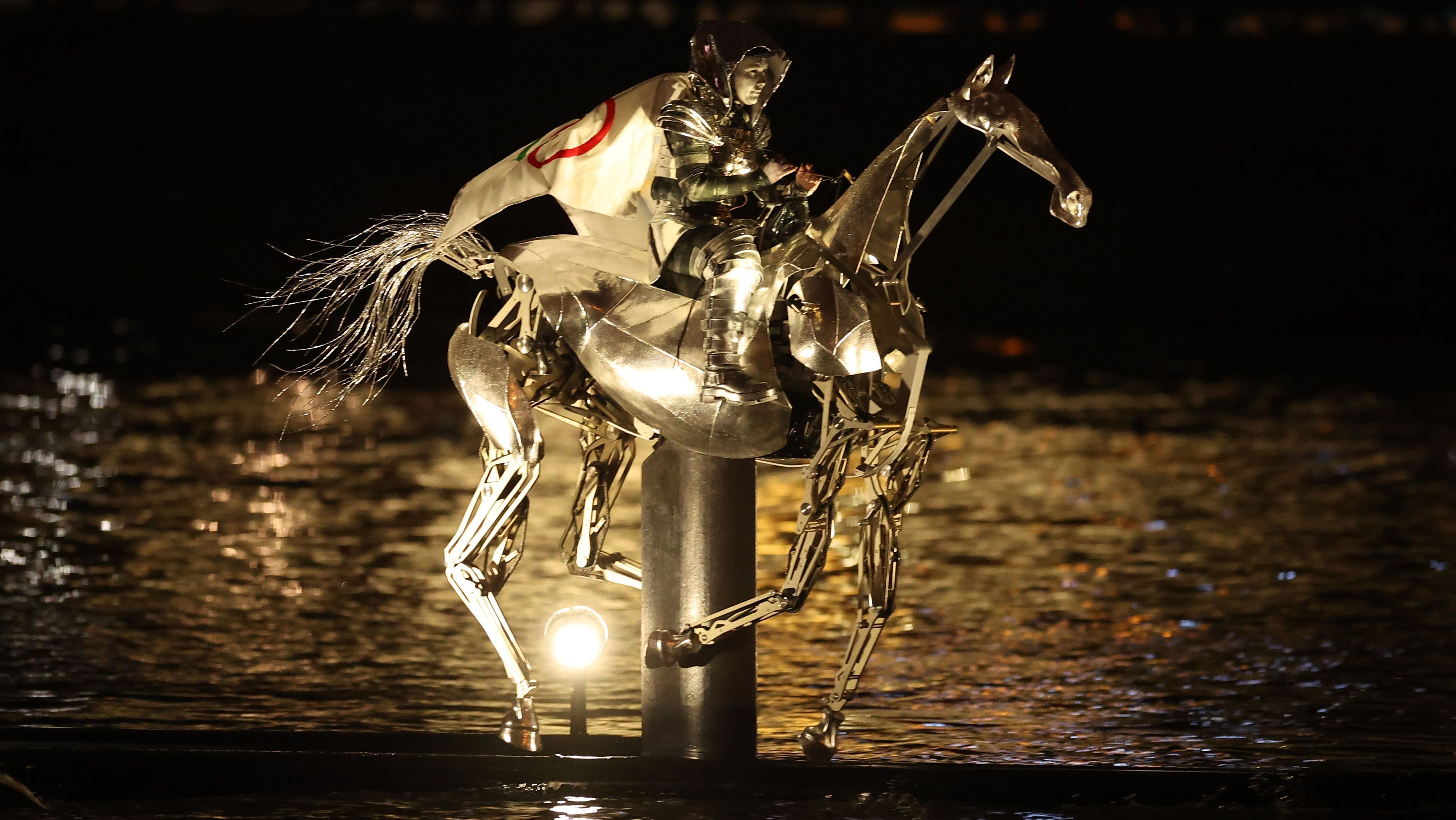 Cavaleiro portador da tocha cavalga pelo rio Sena em um cavalo de metal com a bandeira olímpica / Richard Pelham/Getty Images