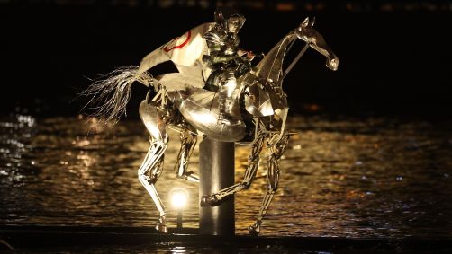 Cavaleiro portador da tocha cavalga pelo rio Sena em um cavalo de metal com a bandeira olímpica