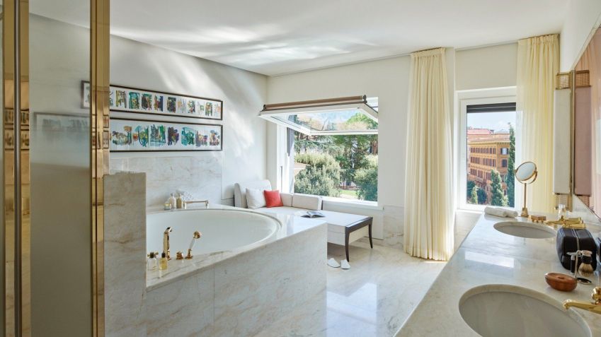 O banheiro de mármore branco e detalhes em ouro tem um chuveiro com efeito de chuva e uma banheira de imersão com vistas para Roma / Dorchester Collection