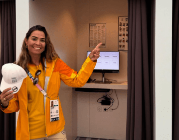 Isabel veste roupa laranja segura um boné branco é loira e sorri