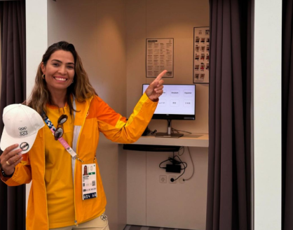 Isabel veste roupa laranja segura um boné branco é loira e sorri