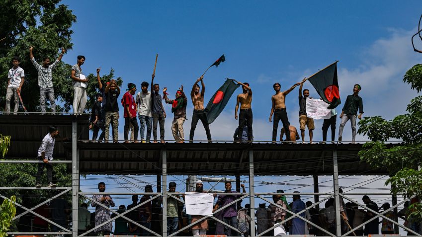 Manifestantes agitam bandeiras nacionais enquanto estão de pé sobre a ponte pedonal em Shahbagh durante um protesto em Dhaka, Bangladesh, em 4 de agosto de 2024, para exigir justiça para as vítimas presas e mortas na recente violência nacional durante os protestos anticotas / Zabed Hasnain Chowdhury/NurPhoto via Getty Images