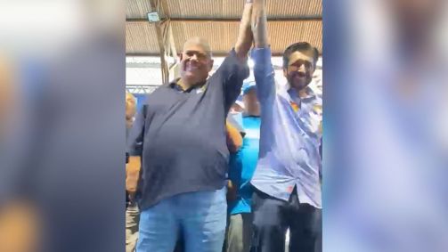 Milton Leite segura a mão de Ricardo Nunes. Ela é moreno, corpulento e veste uma camisa cinza. Nunes é magro, branco, tem barba e veste uma camiseta azul clara.