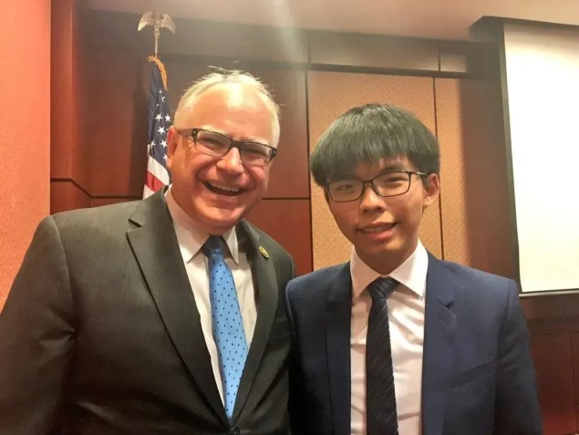 Tim Walz posa para uma foto com o ativista pró-democracia de Hong Kong, Joshua Wang, agora preso. /