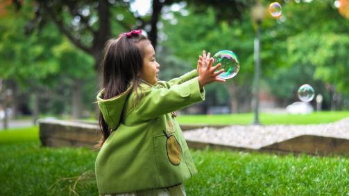 Menina brinca com bolha de sabão em parque