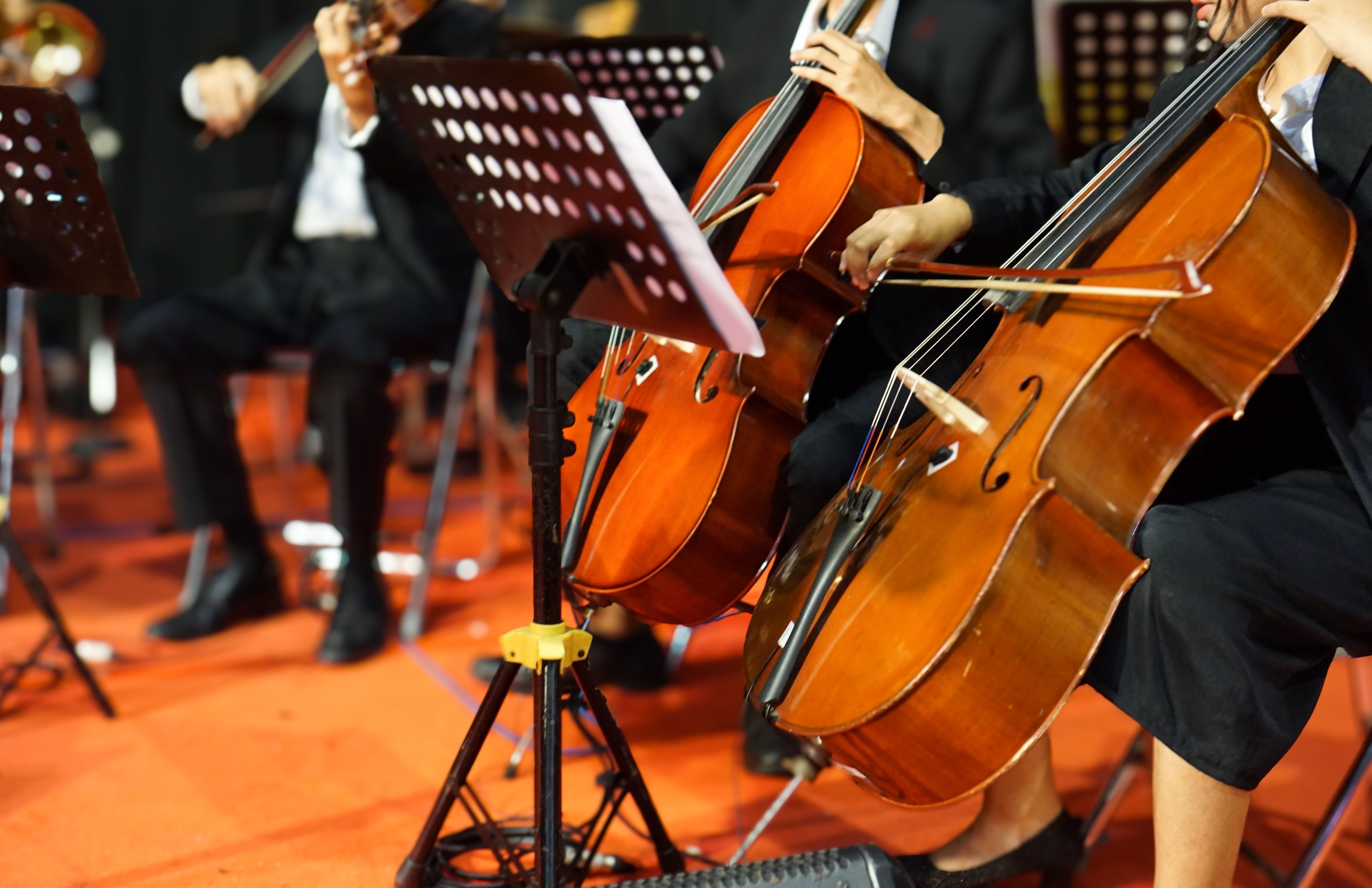 Hands playing cello orchestra with note sheet on stage.