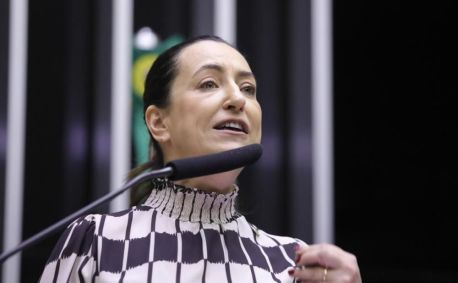Rosangela Mouro é branca e tem o cabelo castanho preso para trás. Tem olhos claros e veste uma camisa estampada.