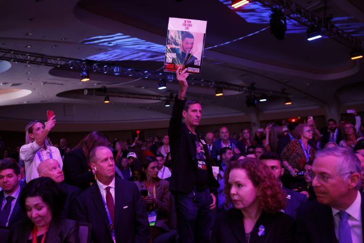 Um membro da plateia segura um pôster enquanto o candidato presidencial republicano, ex-presidente dos EUA, Donald Trump, fala na Cúpula Nacional do Conselho Israelense Americano no Washington Hilton em 19 de setembro de 2024 • Kevin Dietsch/Getty Images