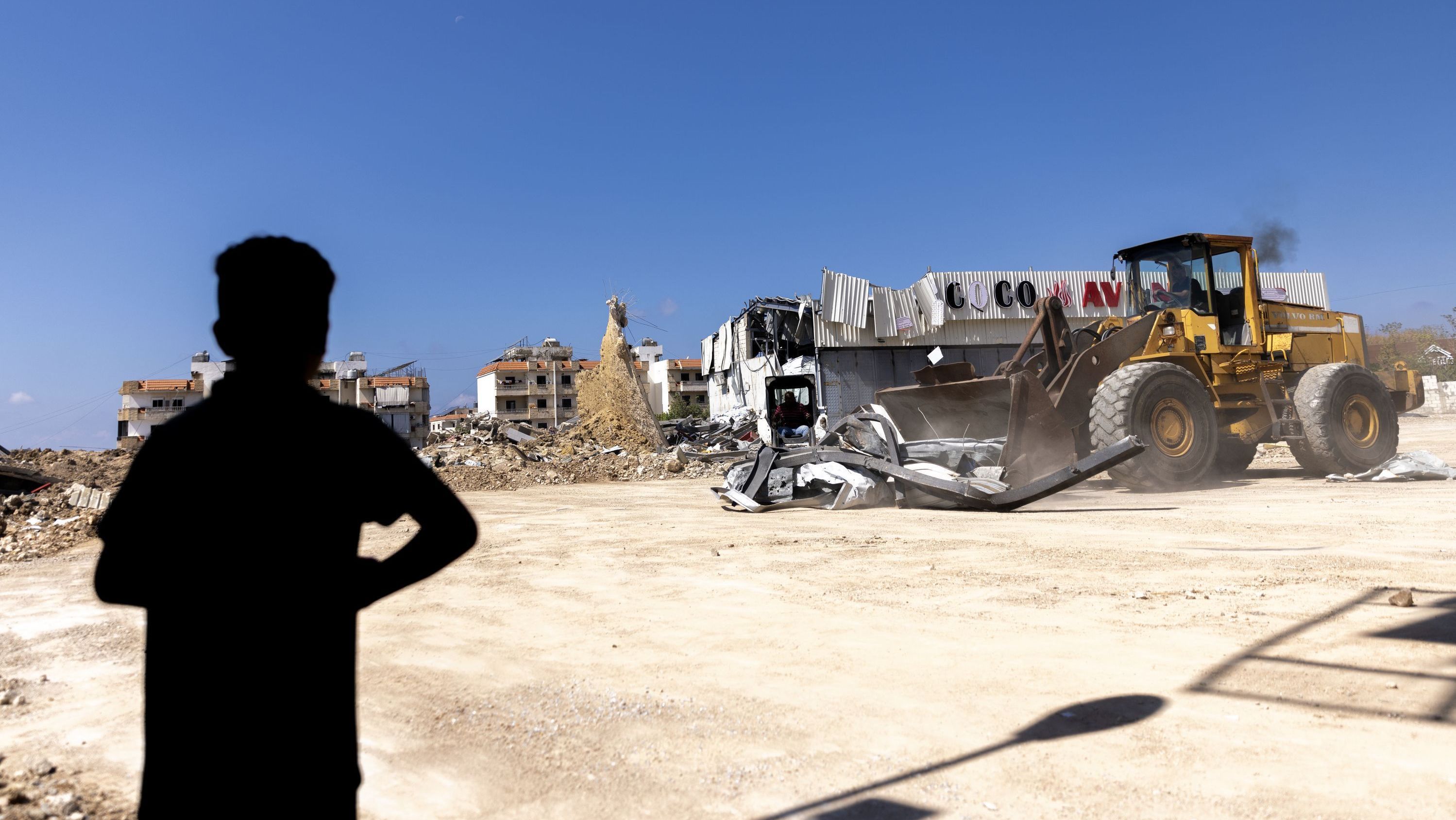 Criança observa escavadeira os destroços após ataque aéreo israelense atingir uma oficina mecânica de veículos em 25 de setembro de 2024 em Jiyeh, no Líbano