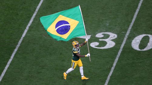 Jaire Alexander, do Green Bay Packers, corre com a bandeira do Brasil durante partida