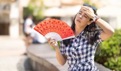 Woman uses hand fan to cool down when summer heat wave hits the city.