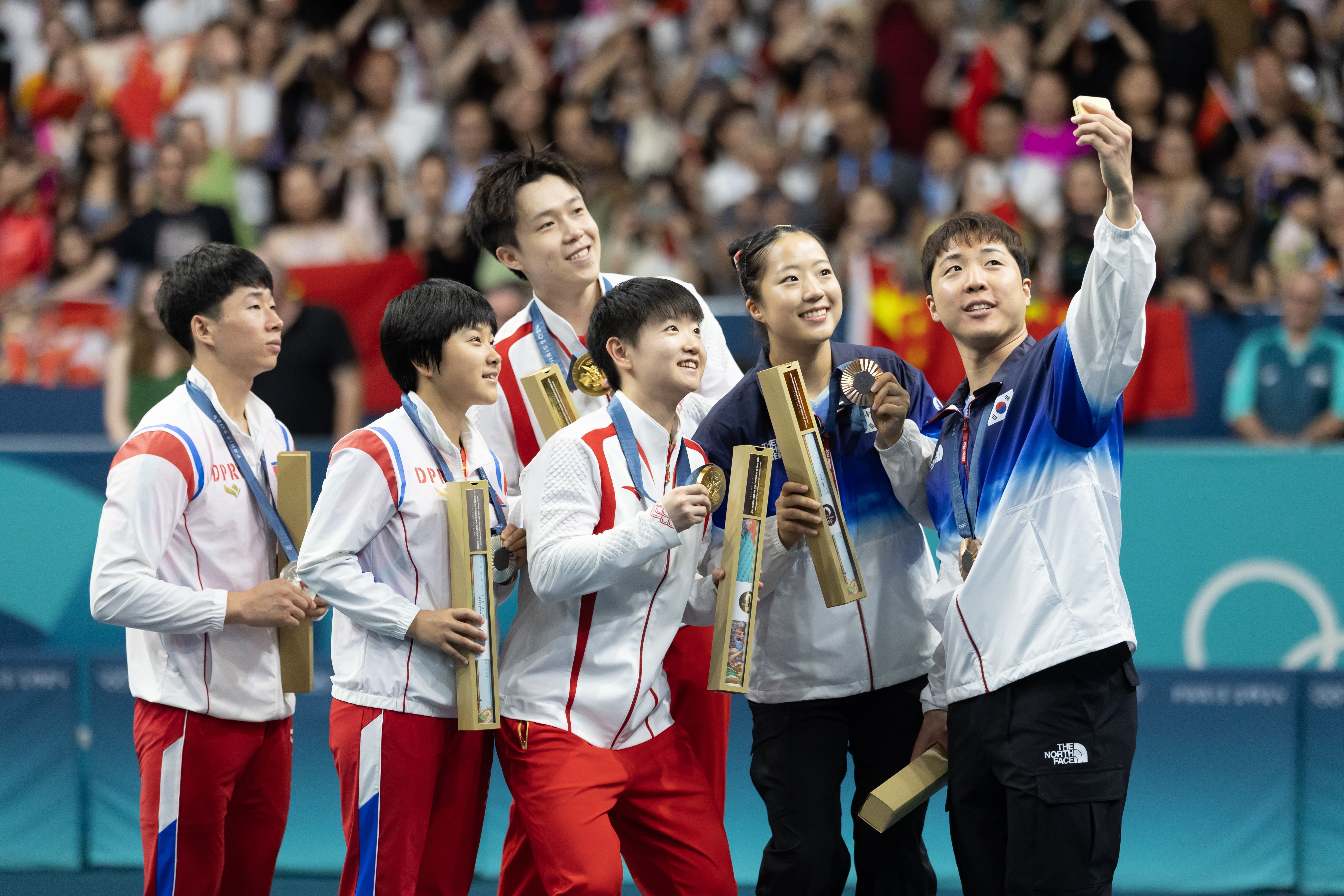 Os chineses Wang Chuqin e Sun Yingsha, medalhistas de ouro, os norte-coreanos Ri Jong Sik e Kim Kum Yong, medalhistas de prata, e os sul-coreanos Lim Jonghoon e Shin Yubin, medalhistas de bronze, tiraram uma selfie no pódio do tênis de mesa masculino em duplas