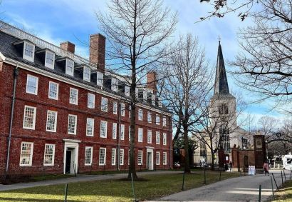 Fachada da Universidade de Harvard, nos Estados Unidos. O prédio é marrom, branco e preto. Há uma torre branca e preta no fundo.