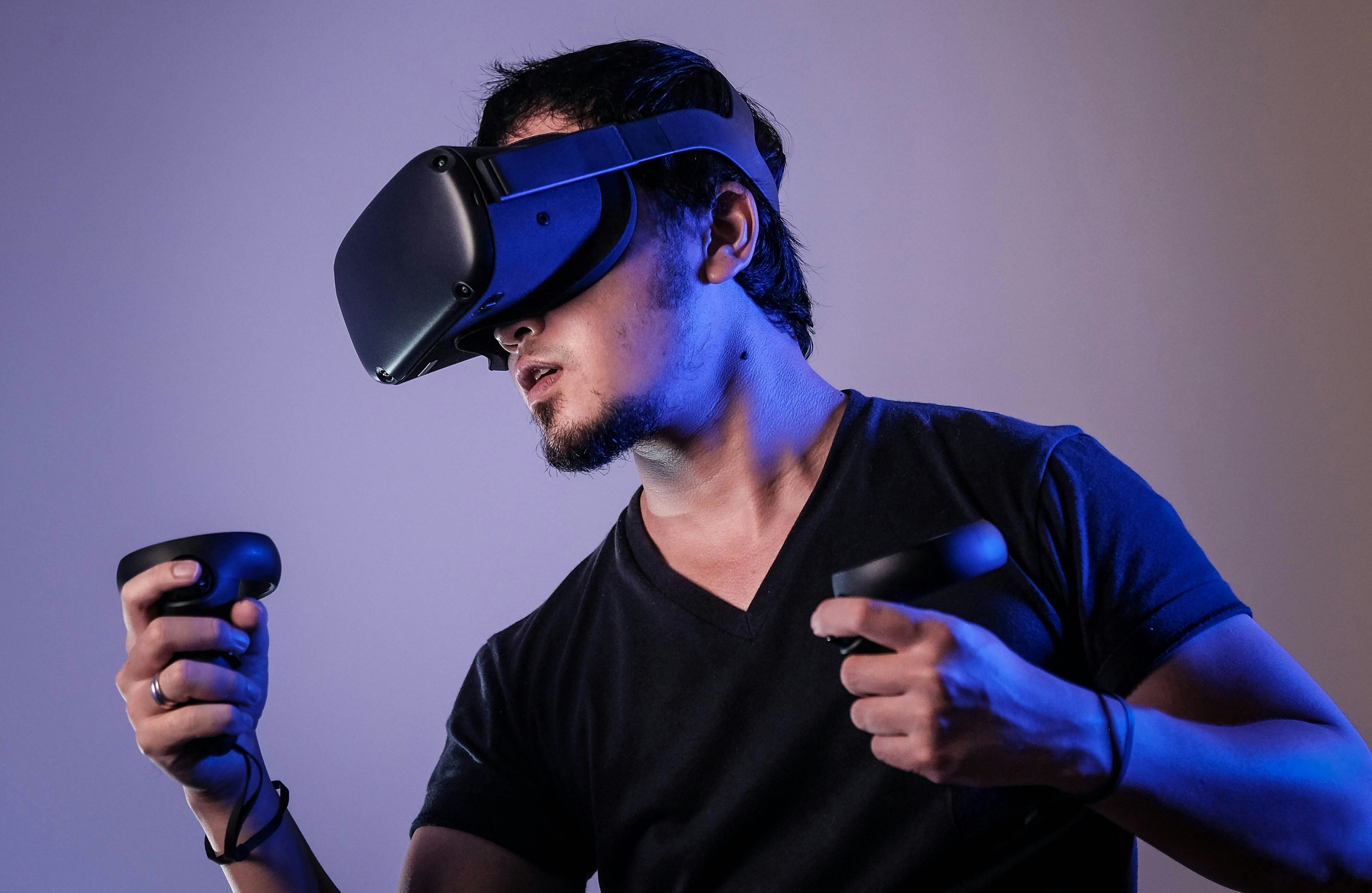 A fotografia apresenta um homem utilizando um óculos de realidade virtual e controles.