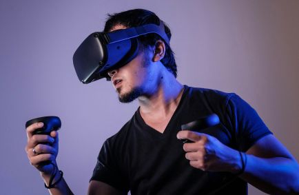 A fotografia apresenta um homem utilizando um óculos de realidade virtual e controles.