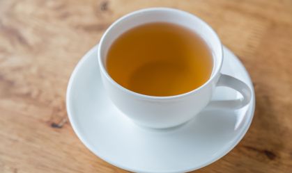 Xícara com chá amarelado em mesa