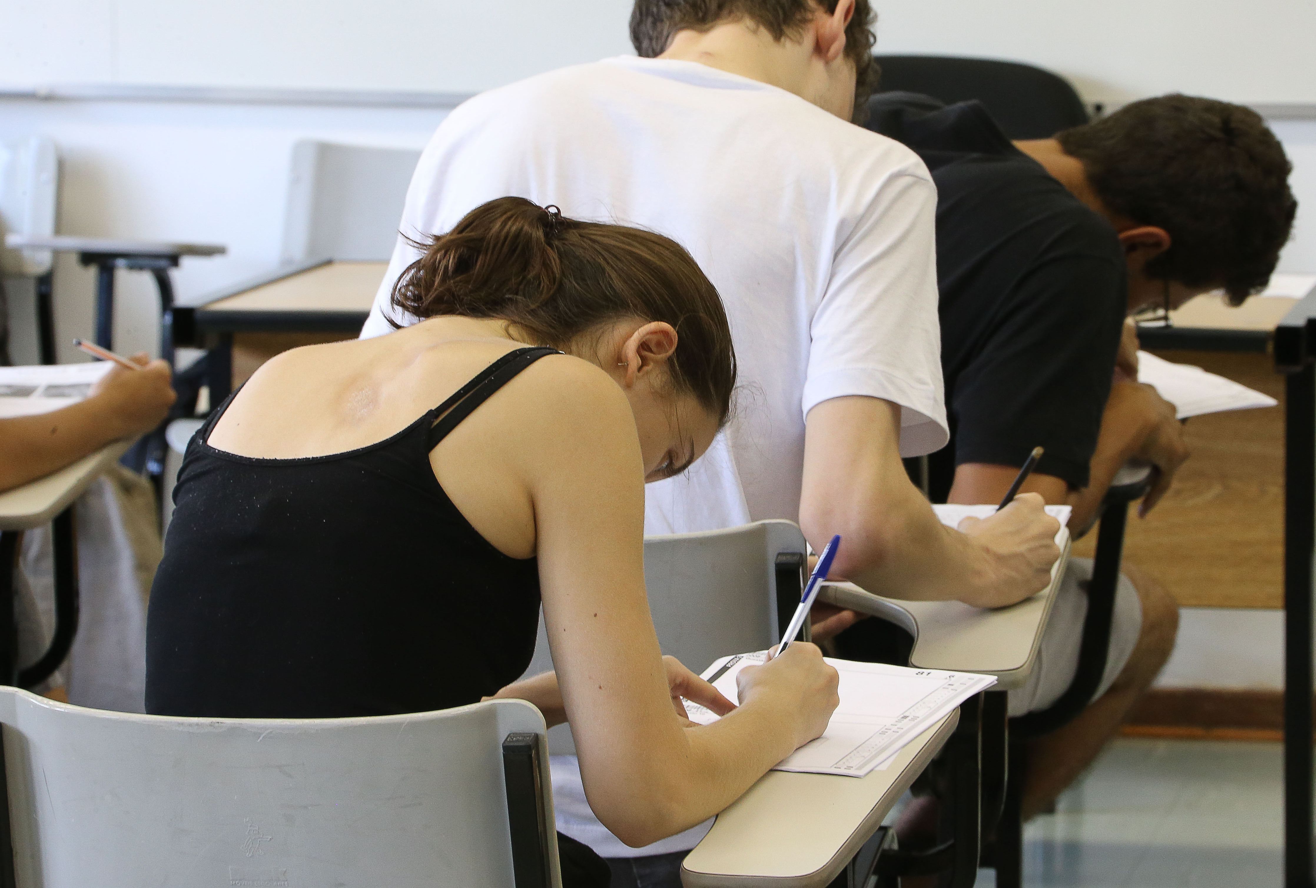 Jovens realizando prova de vestibular. Eles estão sentados e escrevendo.