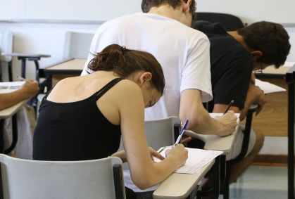 Jovens realizando prova de vestibular. Eles estão sentados e escrevendo.